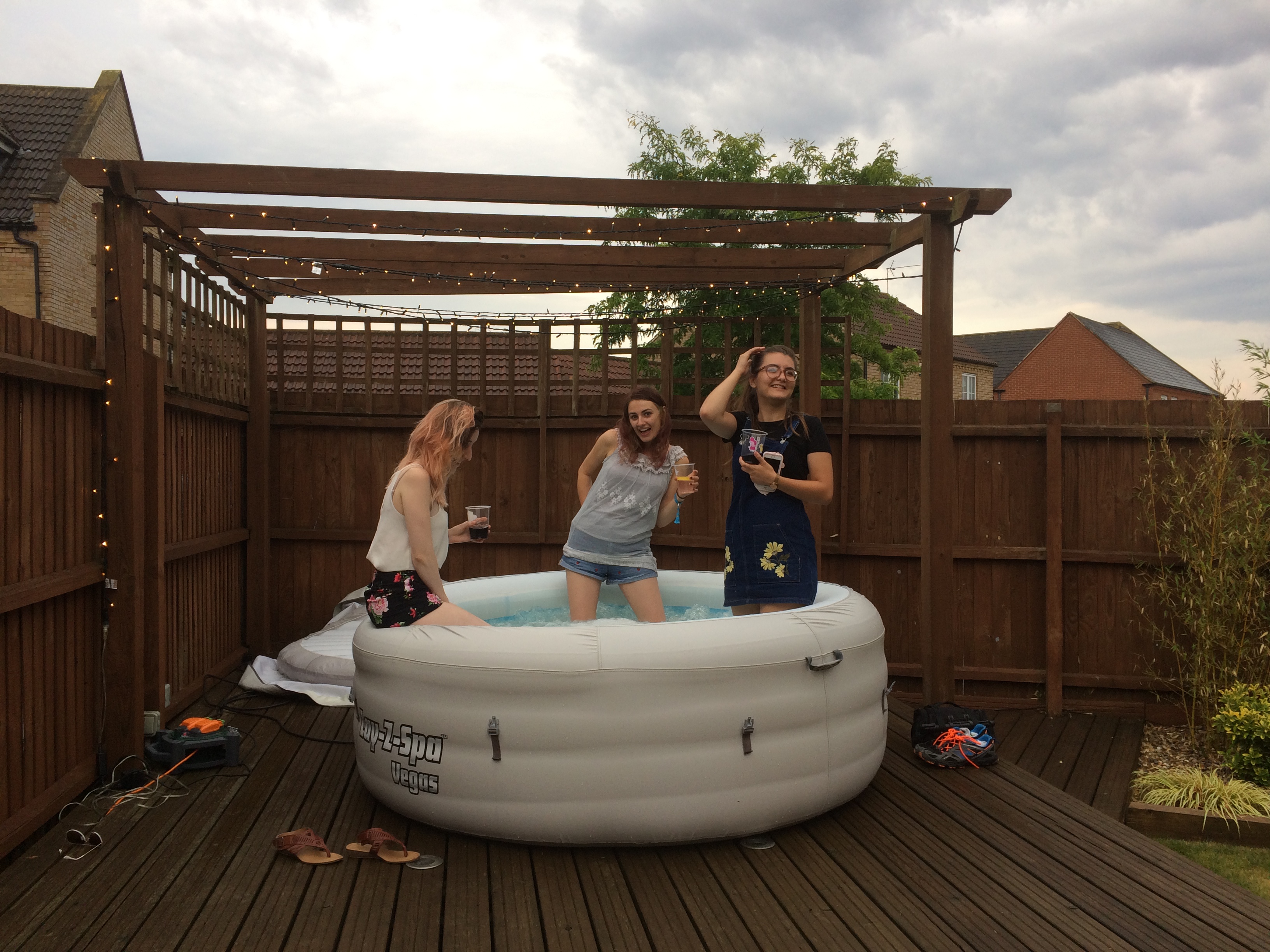 Alice, Lauren and Berni perched at the edge of the hot tub with their legs in the water, under a grey sky