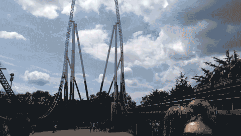 GIF of a roller coaster cart launching very fast from the right of the view and climbing a tall arc before slowly going over the top and coming back down - the climb and drop are almost straight up and down. It's so tall the camera has to move to fit it in when the coaster is at the top.